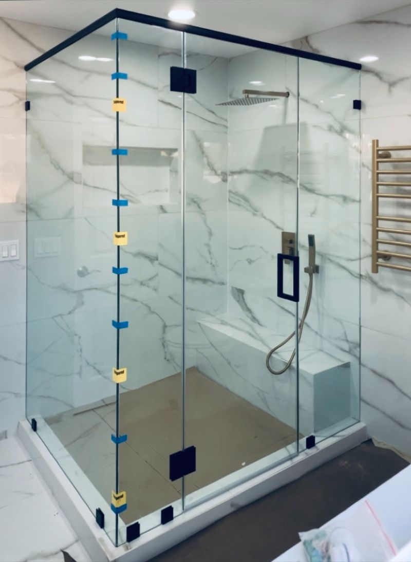 Frameless matte-black multi-panel shower enclosure with a top header installed in Anaheim