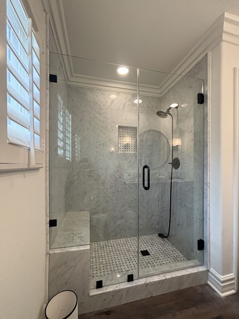 Finished frameless shower door and fixed inline panel fitted beside a tiled bench in Irvine
